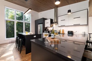 Une cuisine moderne dotée d’un îlot central, d’appareils électroménagers en acier inoxydable et offrant une vue sur l’extérieur.