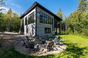 A modern two-story cabin with large windows, outdoor seating, and a gravel driveway. - Maison ULLR | Zen Retreat | 10 min to Le Massif (Petite-Rivière-Saint-François)