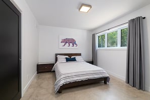 Ein Schlafzimmer mit einem Bett, einem Nachttisch, einem Fenster mit Vorhängen und einem Wandbild von einem Bären.