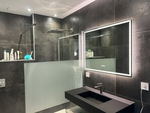 Un baño moderno con un espejo grande, un lavamanos integrado y una zona de ducha.