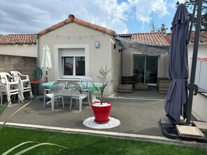 Un patio con mesa y sillas, una maceta roja y una zona de estar cubierta.