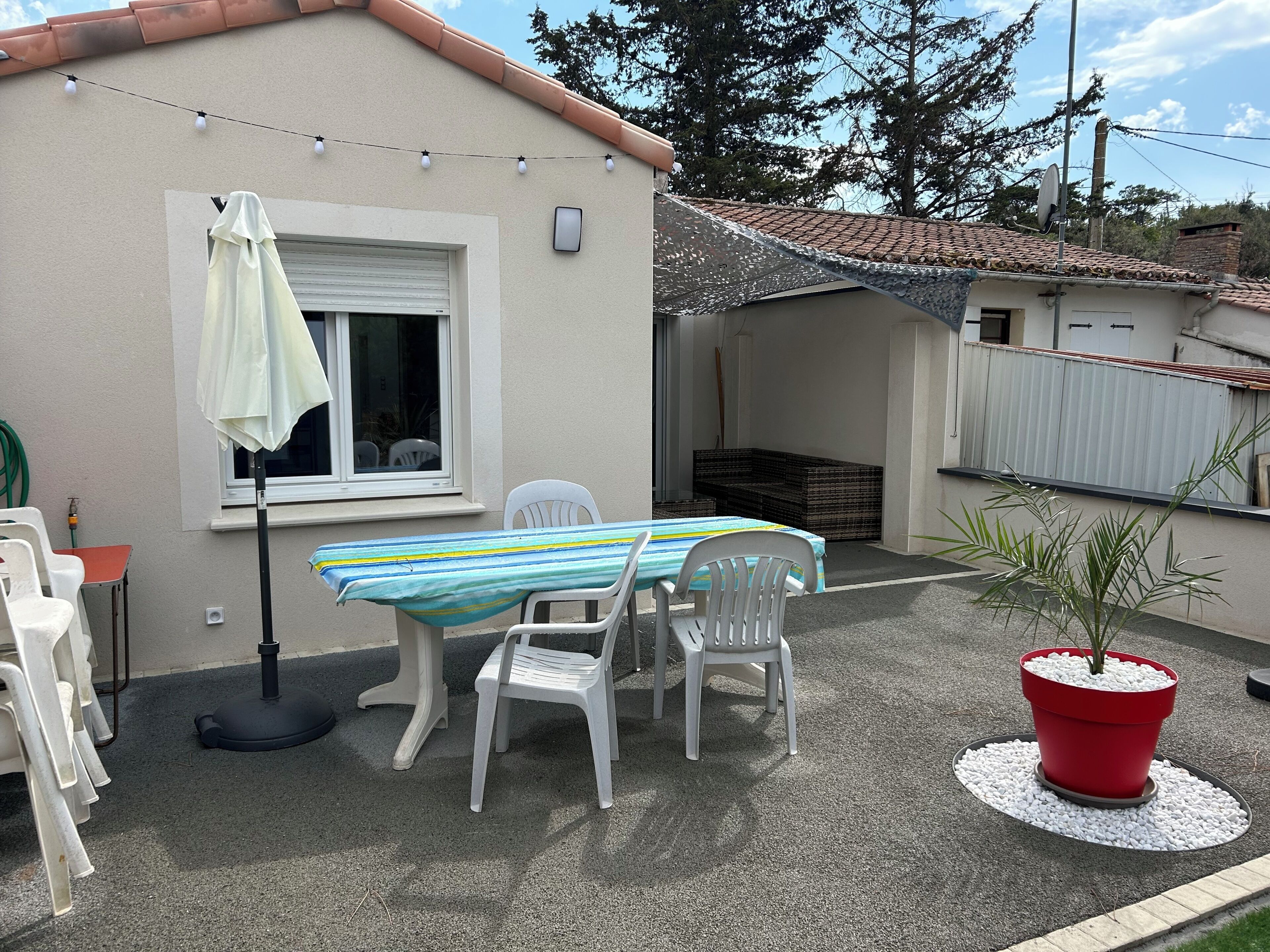 Un'area patio con tavolo e sedie, una pianta in vaso e una ghirlanda di luci.