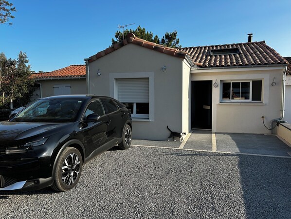 Un edificio residencial con un automóvil estacionado en la entrada, un gato cerca de la puerta y un cielo azul despejado.