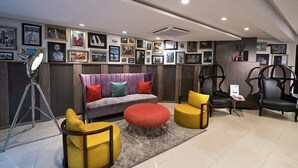 Una sala de estar moderna con un sofá, dos sillones amarillos, un reposapiés rojo y una lámpara con trípode.
