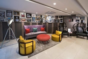 A modern living room with a sofa, two yellow armchairs, a red ottoman, and a tripod lamp. - Maison Hotel By Fahrenheit  (Lagos)