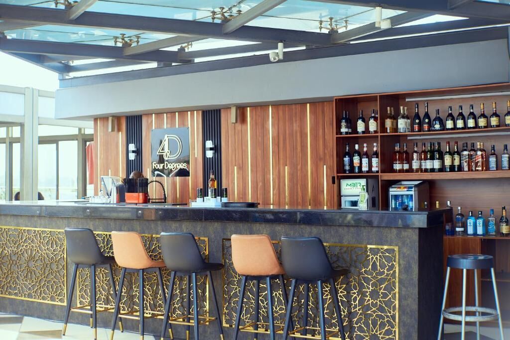 A bar area with a wooden counter, bar stools, and a variety of bottles.