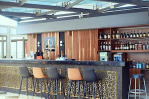 Zona de bar con mostrador de madera, taburetes y una variedad de botellas.