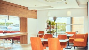 Un comedor moderno con paneles de madera, sillas anaranjadas y un ventanal con vistas al estacionamiento.