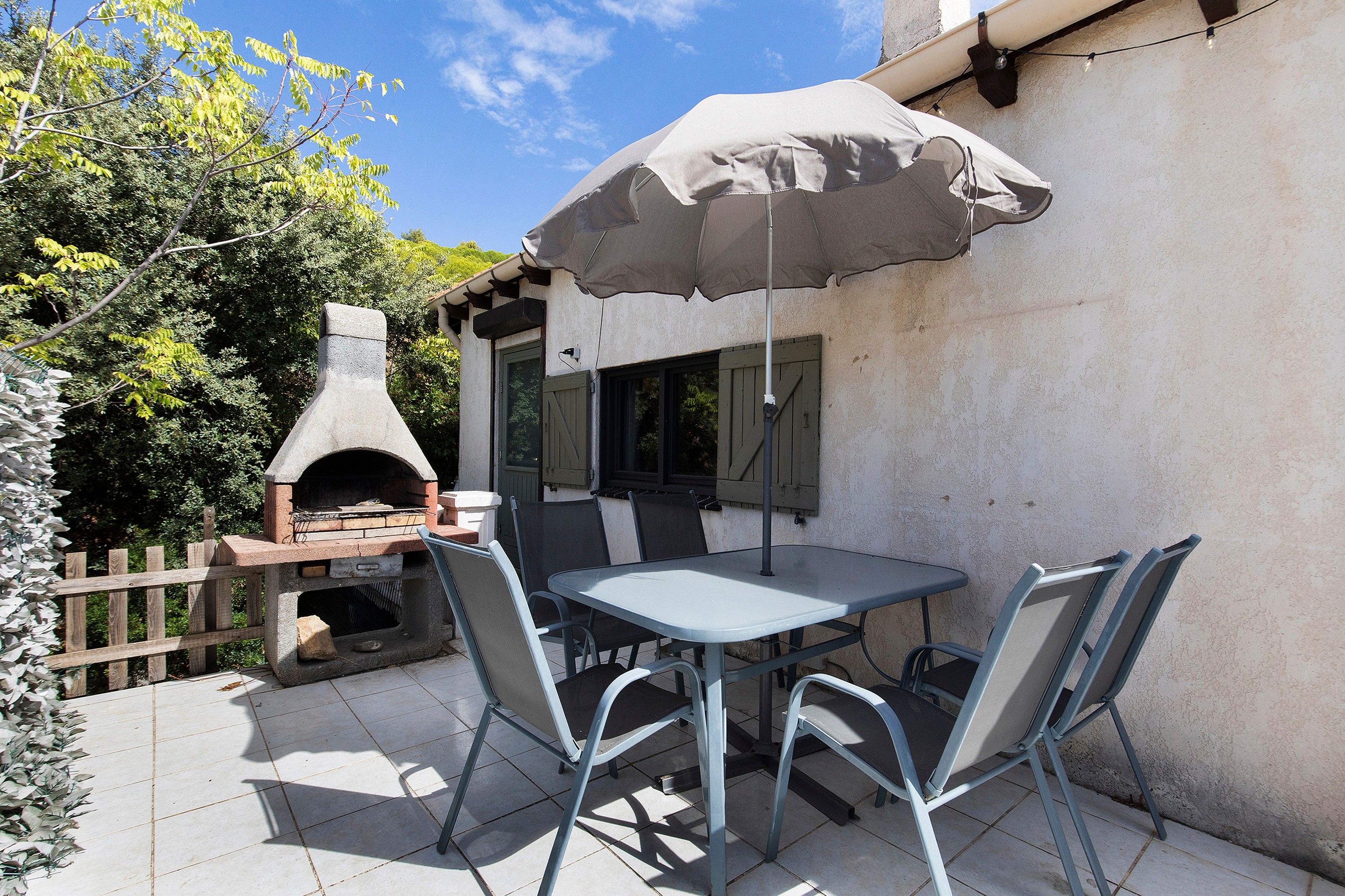 Een terras buiten met een tafel, stoelen, een barbecue en een pergola met een parasol.