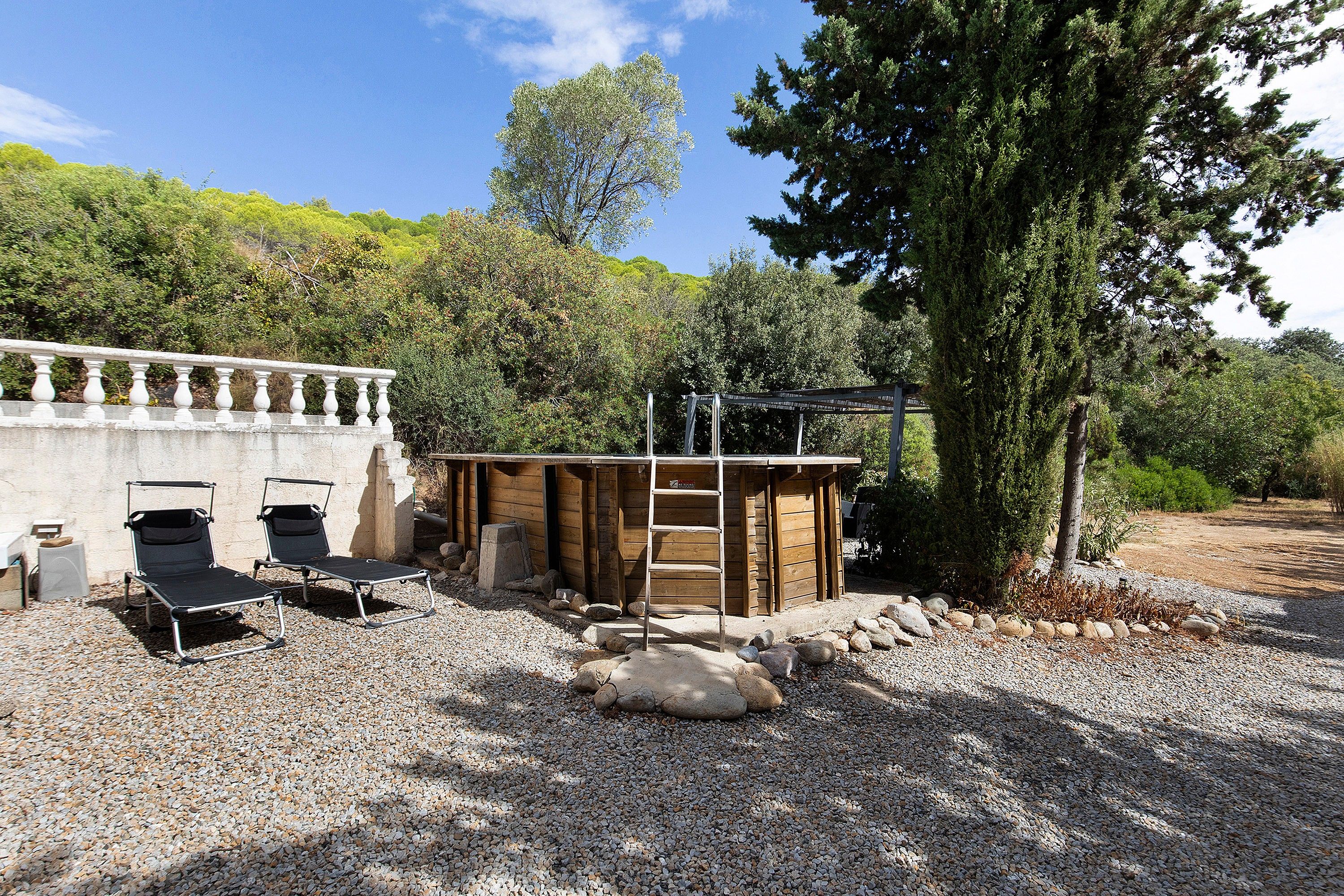 A rustic outdoor area with a wooden structure, a ladder, and two black lounge chairs.