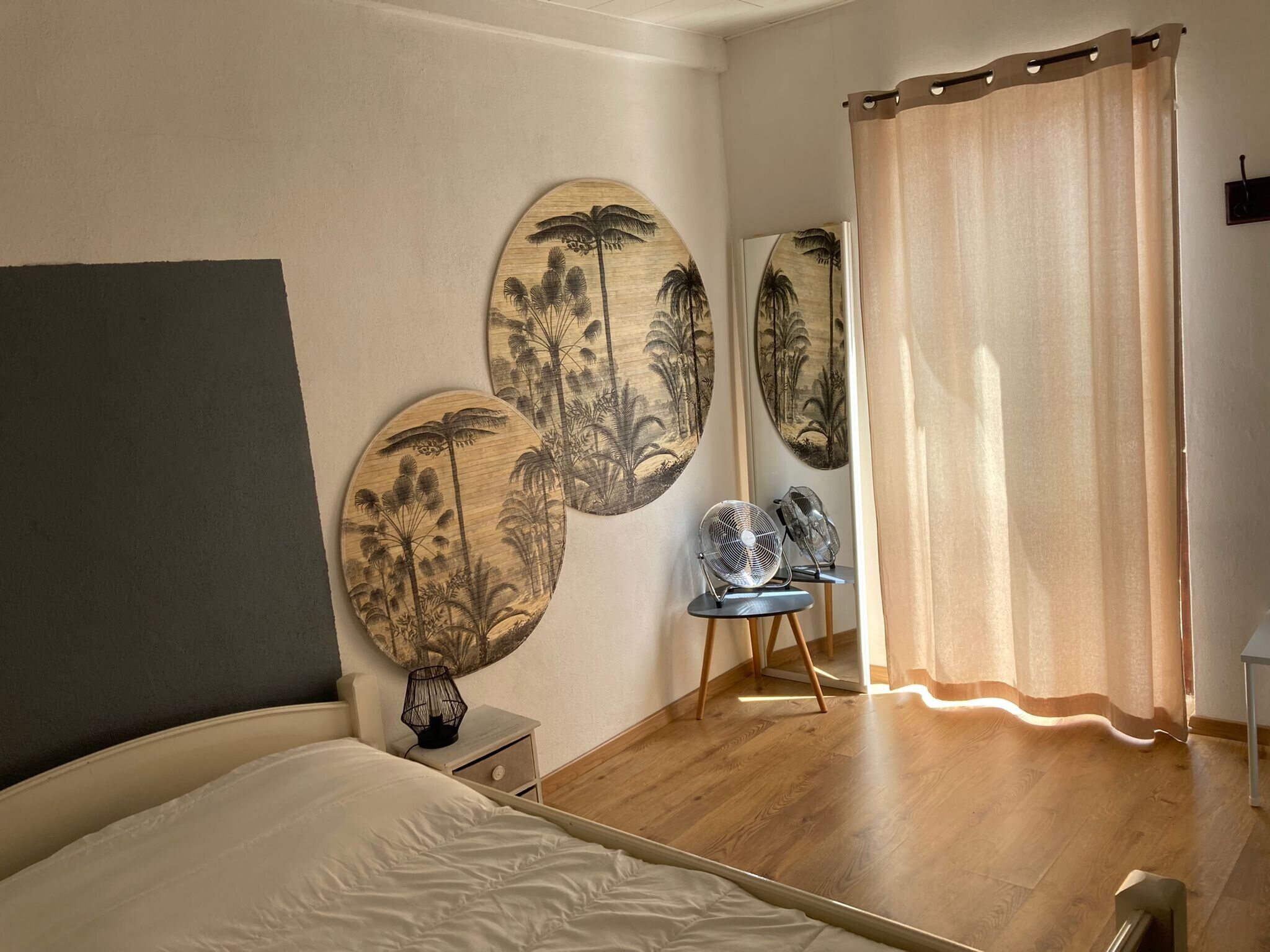 Een slaapkamer met een bed, een stoel, een ventilator en twee decoratieve panelen aan de muur.