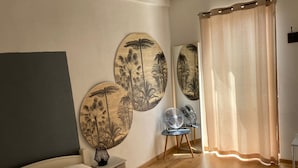 Een slaapkamer met een bed, een stoel, een ventilator en twee decoratieve panelen aan de muur.