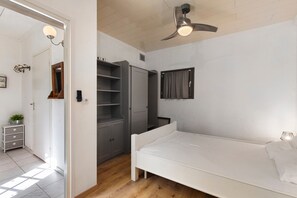 Ein Schlafzimmer mit einem weißen Bett, einem Deckenventilator, einem Kleiderschrank und einem kleinen Fenster mit Vorhängen.
