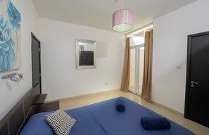 A bedroom with a bed, a mirror, a shower, and a door.