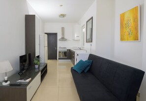 Un salon moderne avec un canapé noir, un téléviseur et une petite table sur laquelle se trouvent une lampe et une télécommande.