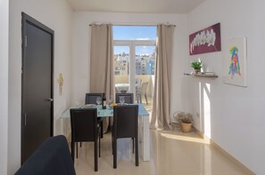 Een eetgedeelte met een tafel gedekt voor twee personen, een raam met gordijnen en uitzicht op gebouwen.