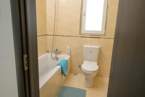 Een badkamer met een bad, toilet en een raam boven het toilet.