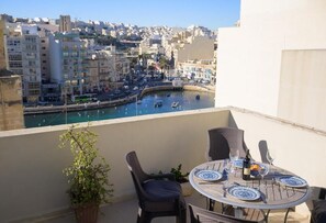 Een balkon met een eettafel, met uitzicht op een haven met boten en gebouwen.