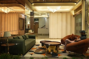 Un área de descanso moderna con un sofá verde, sillones naranjas y un tapete estampado.