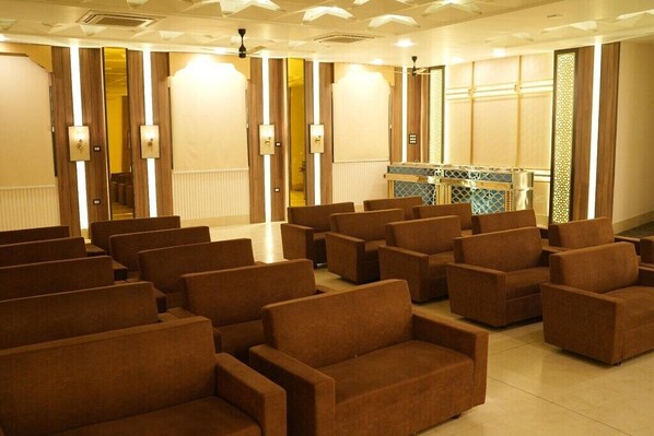 A conference room with rows of brown chairs, a reception desk with a patterned backdrop, and a wooden partition with vertical light fixtures.