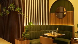 Een restaurant met een groene zithoek met banken, een wand van houten latten en een ronde spiegel.