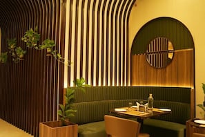 Un restaurante con zona de asientos en un asiento verde tipo cabina, pared de listones de madera y un espejo redondo en la pared.