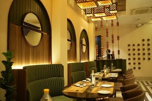 A restaurant with round tables, green upholstered booths, and a wall with circular patterns.