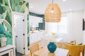 Een moderne keuken met witte kasten, een blauwgroene achterwand en een eethoek met een tafel en stoelen.