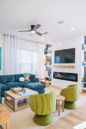 Een moderne woonkamer met een bank, groene stoelen, een salontafel, een flatscreen televisie en een open haard.
