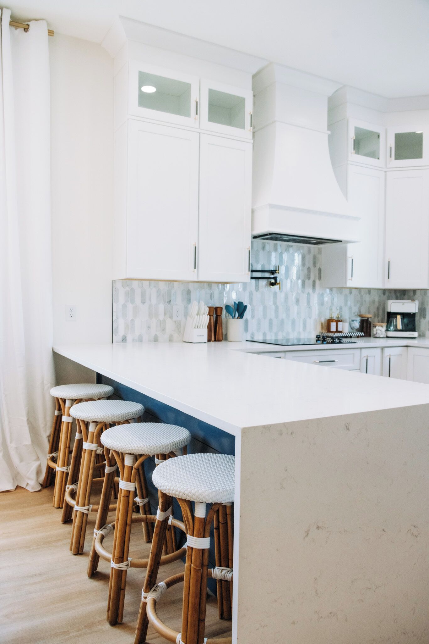 Une cuisine moderne avec des meubles blancs, un grand îlot central doté de tabourets et un crédence décorée de motifs.
