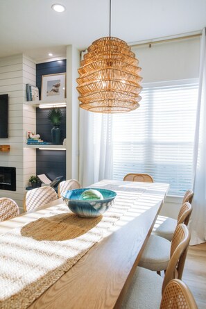A dining area with a wooden table, woven pendant light, and wicker chairs. - The Cove Reunion HQ - Sleeps 22 - Gym - Game Room - Theater - Spa (Santa Rosa Beach)