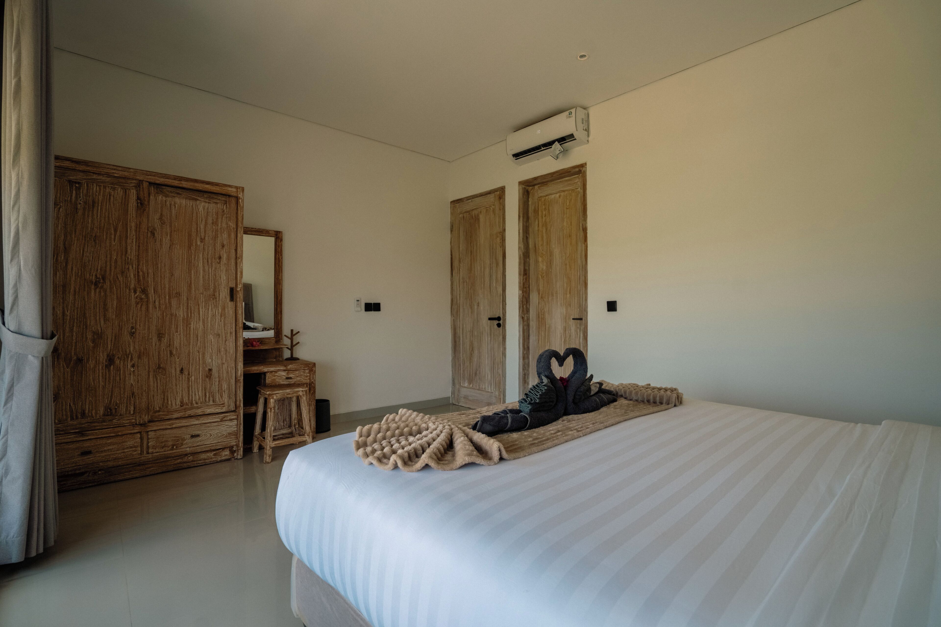 A hotel room with a large bed, wooden wardrobe, and a mirror.