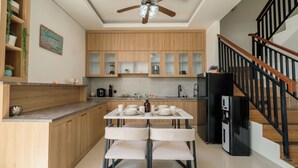 A modern kitchen with wooden cabinets, a dining table with chairs, a black refrigerator, and a staircase with wooden railings. - Villa Lopina Umalas (Kuta Utara)