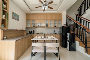 Una cocina moderna con armarios de madera, una mesa de comedor con sillas, un refrigerador negro y una escalera con barandillas de madera.