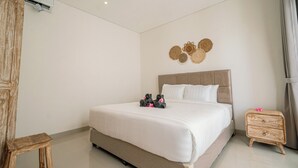 A hotel room with a large bed, a wooden nightstand, a wall-mounted air conditioner, and a decorative wall piece. - Villa Lopina Umalas (Kuta Utara)