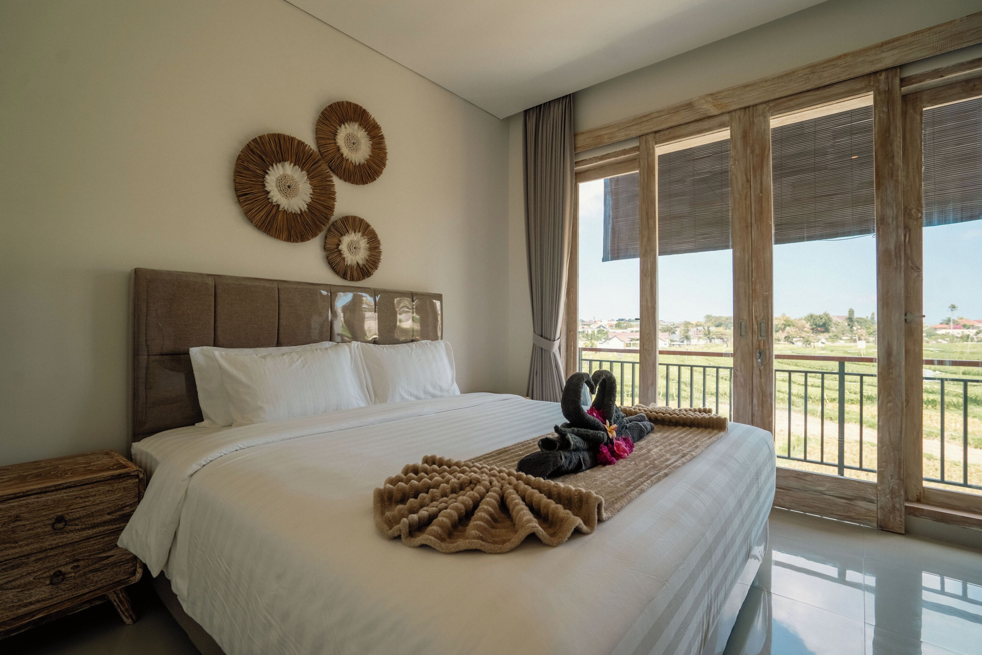 Habitación de hotel con una cama grande, cabecero de madera y vistas al exterior a través de amplios ventanales.