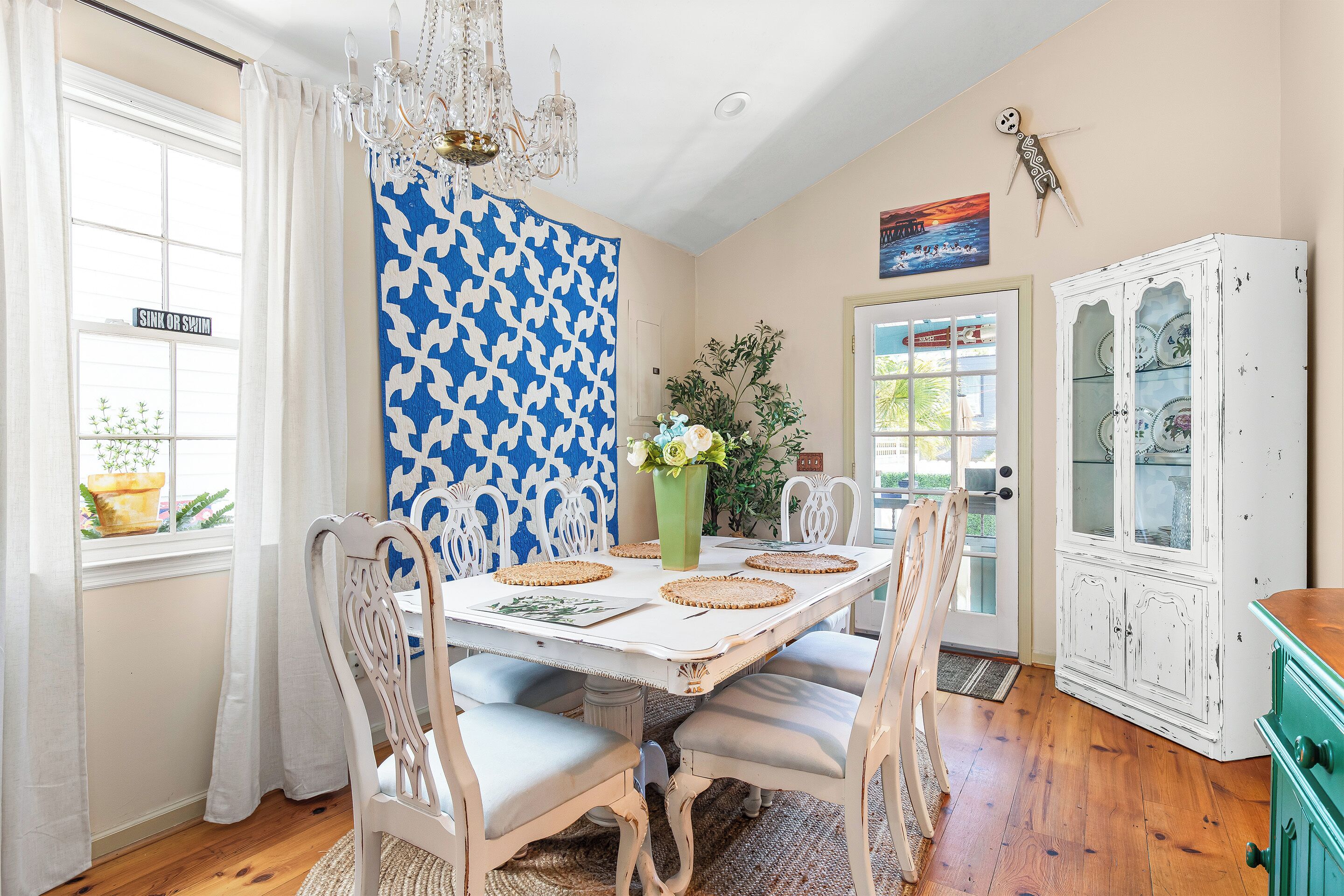 Comedor con una mesa blanca, pared con diseño azul y una lámpara de araña.