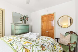 A bedroom with a bed, dresser, mirror, and a door. - Blue Water Cottage | Porch, Courtyard, Office by Lucky Savannah (Savannah)