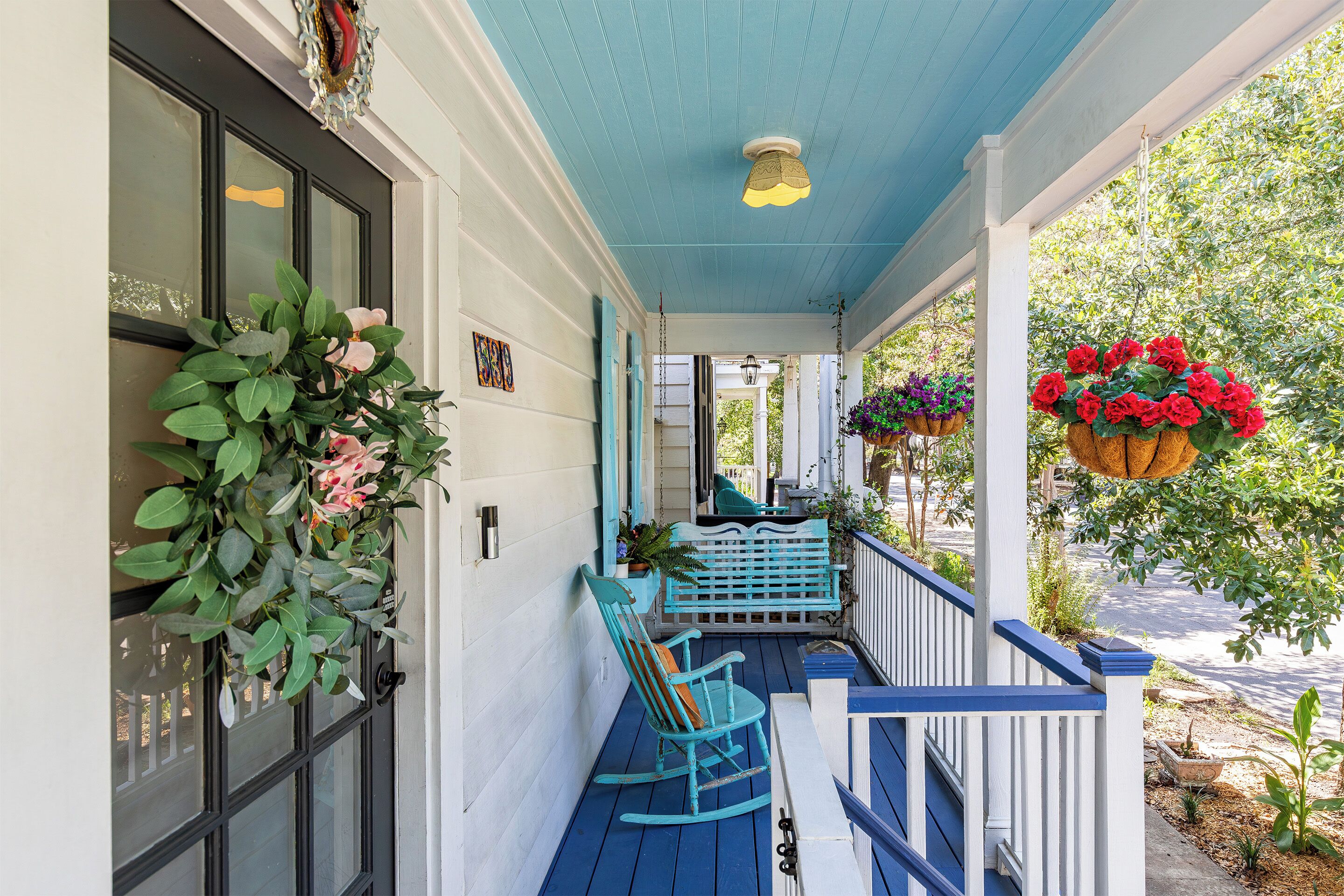 A porch with a blue railing, a bench, and hanging flower baskets.