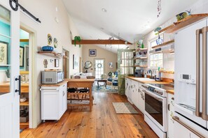 A kitchen with wooden flooring, white cabinets, a microwave, a stove, and various kitchen utensils. - Blue Water Cottage | Porch, Courtyard, Office by Lucky Savannah (Savannah)