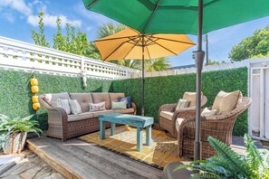 A patio area with a sofa set, chairs, a table, and an umbrella. - Blue Water Cottage | Porch, Courtyard, Office by Lucky Savannah (Savannah)