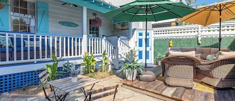 A covered patio area with outdoor furniture, a wooden table, and a wicker sofa.