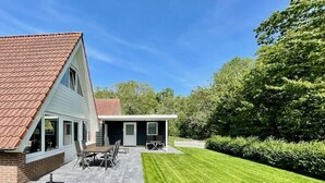 Una casa a due piani con patio, zona pranzo e cucina esterna coperta.