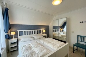 A bedroom with a bed, bedside tables, a mirror, and a chair. - Holiday home with 3 bedrooms (Oostkapelle)