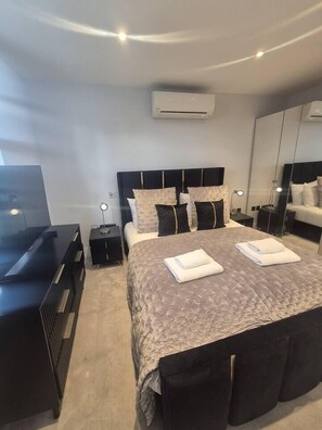 A modern bedroom with a large bed, bedside tables, a TV, and a mirror. - Elegant Sloane Gate Residence | 2 Bed - 2 Bath (Greater London)