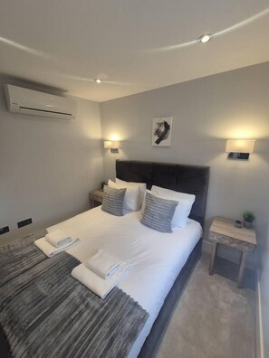 Ein modernes Hotelzimmer mit einem großen Bett, zwei Nachttischen, einer Wandklimaanlage und einer Deckenleuchte.