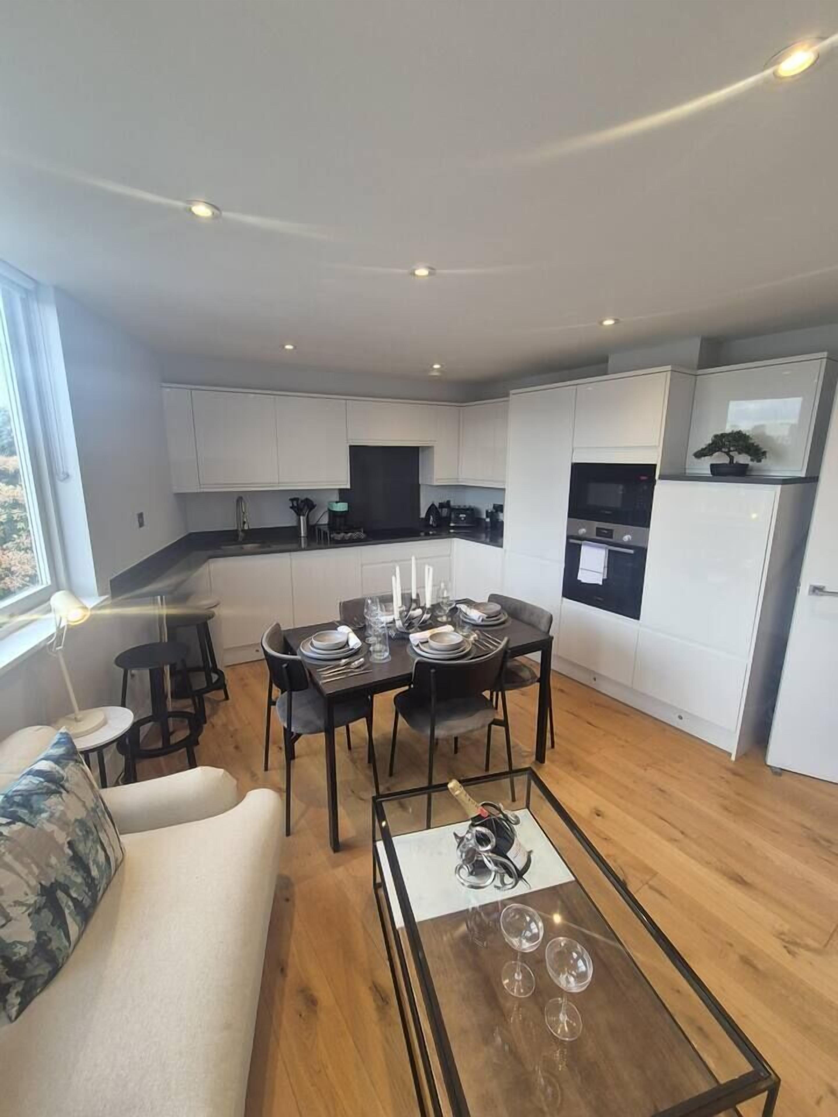 A modern kitchen with white cabinets, a dining area with a round table, and a sofa.