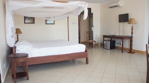 A hotel room with a four-poster bed, a desk with a chair, a television, and an air conditioning unit. - Millennium Sea Breeze Resort (Pwani Bagamoyo)