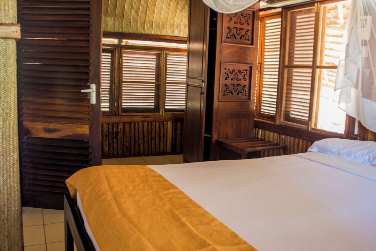 A room with a bed, wooden walls, and a window with blinds.