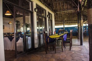 A restaurant with a stone floor, wooden chairs, and a table with a yellow tablecloth. - Millennium Sea Breeze Resort (Pwani Bagamoyo)
